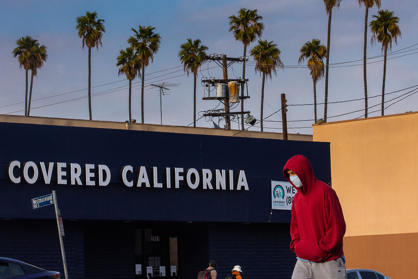 A man with a surgical mask walks in front of a Covered California sign