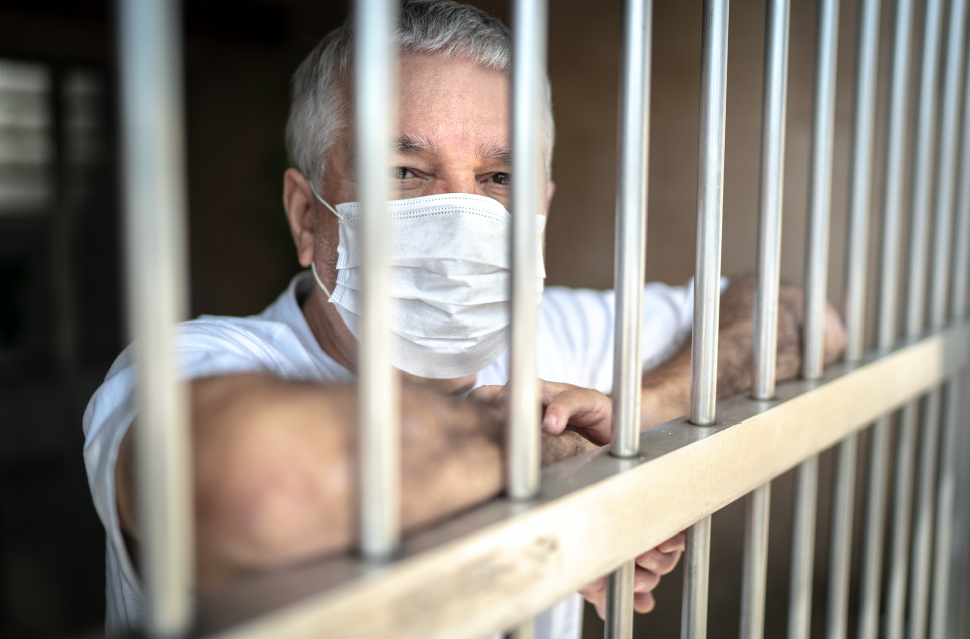 A man with a facemask shown behind bars