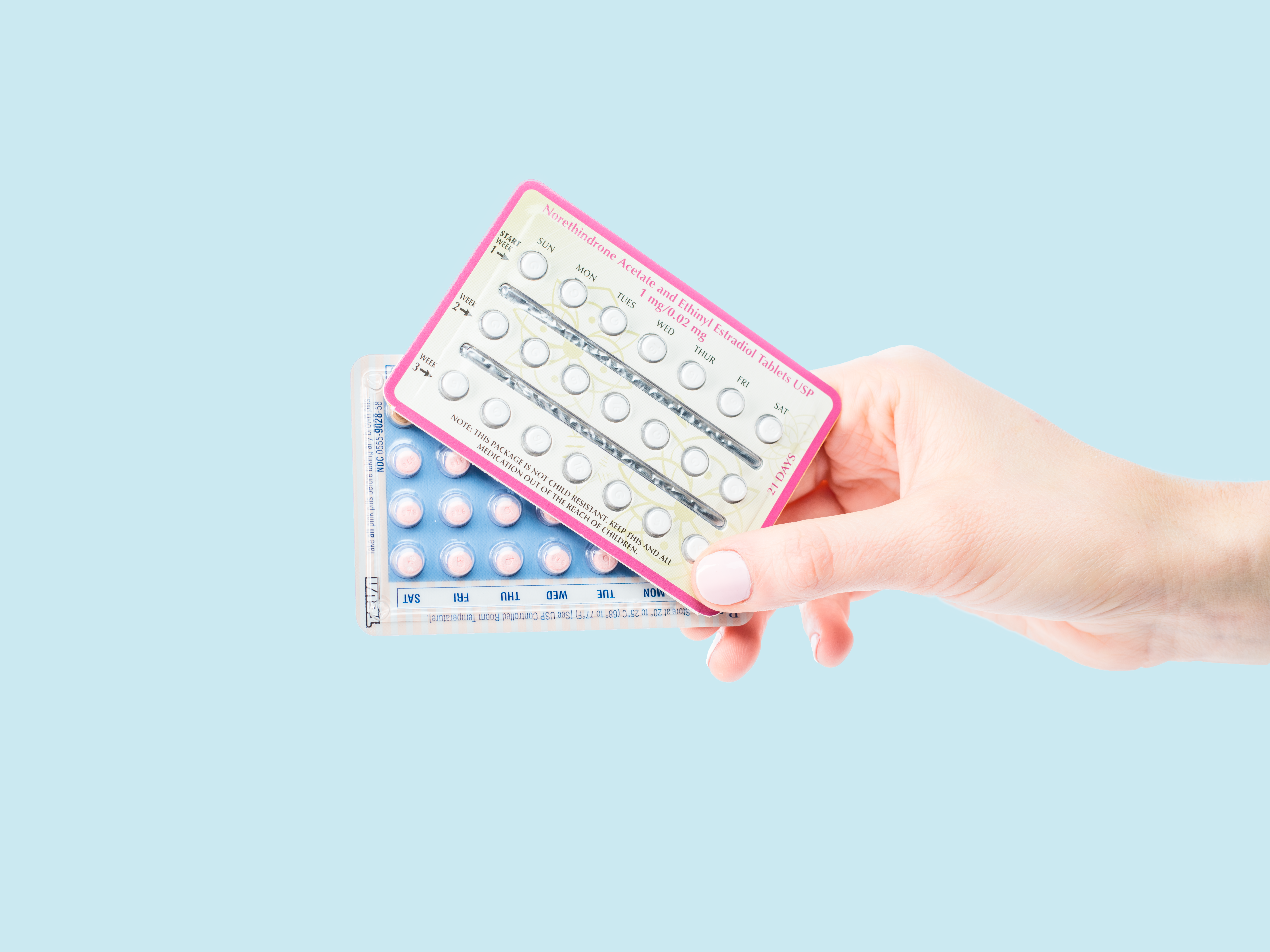 a womans hand holding a packet of birth control pills