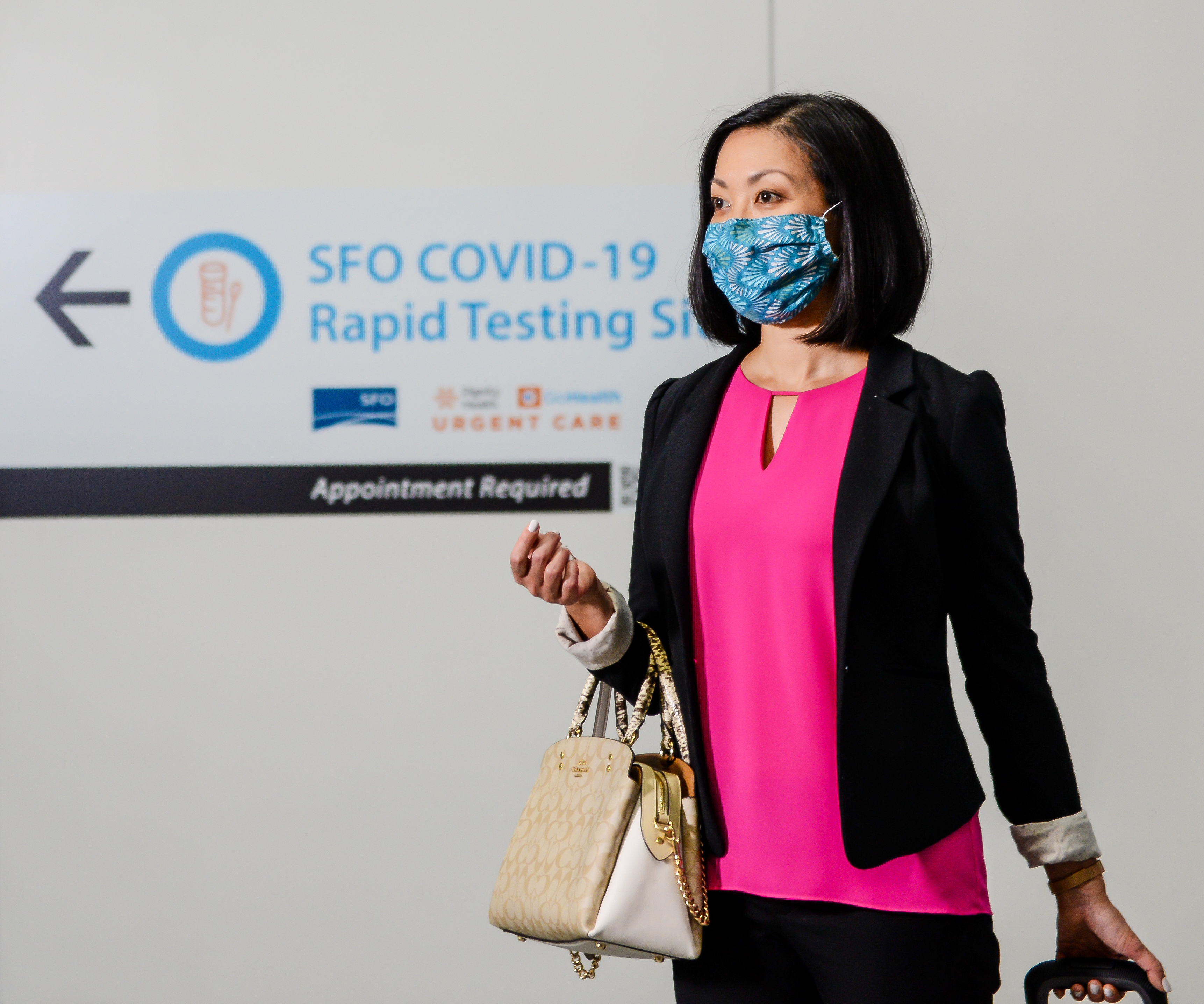 woman wearing a mask walks by a COVID-19 testing site at SFO airport