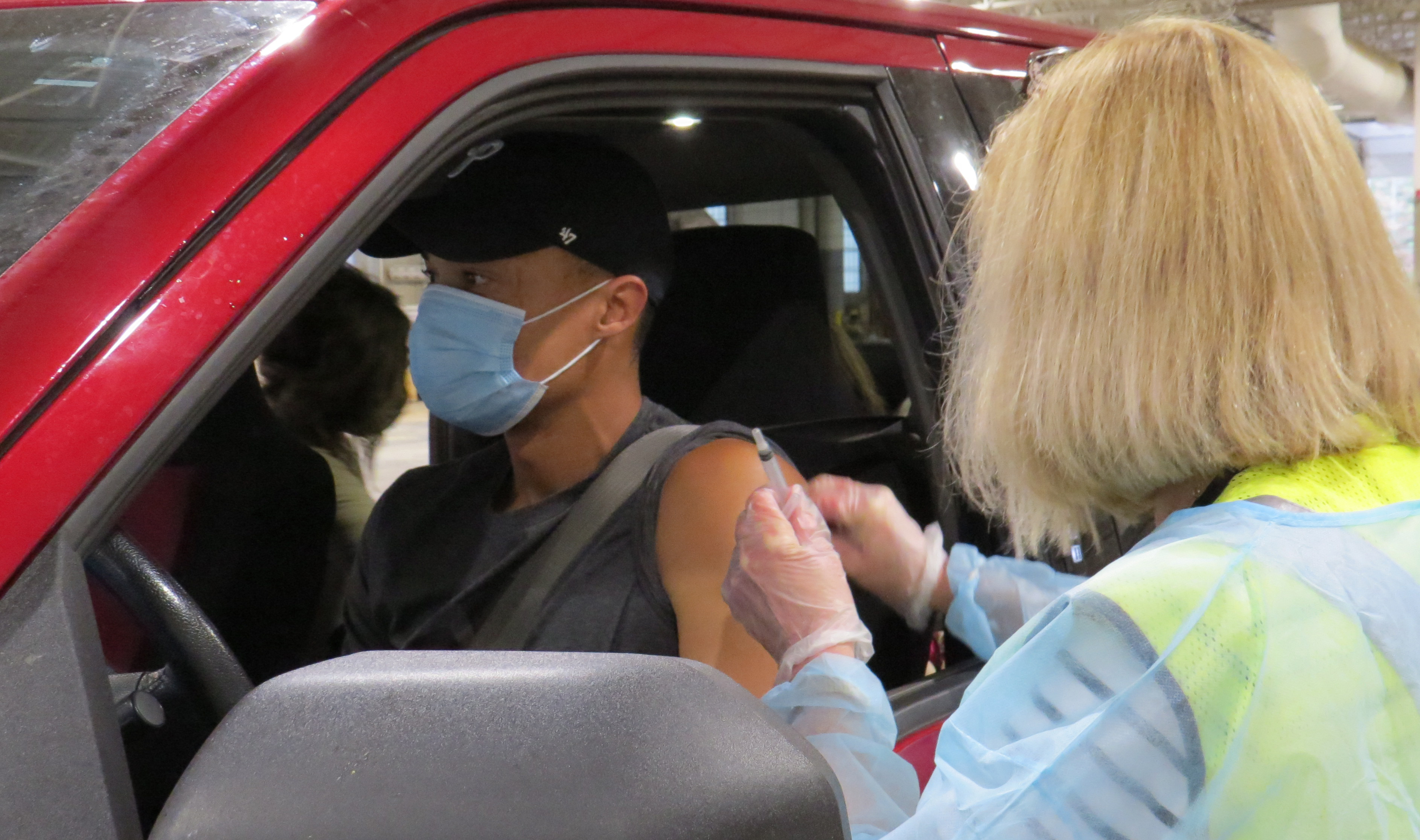 a man in his truck receives a flu vaccine shot from a nurse in a flu clinic