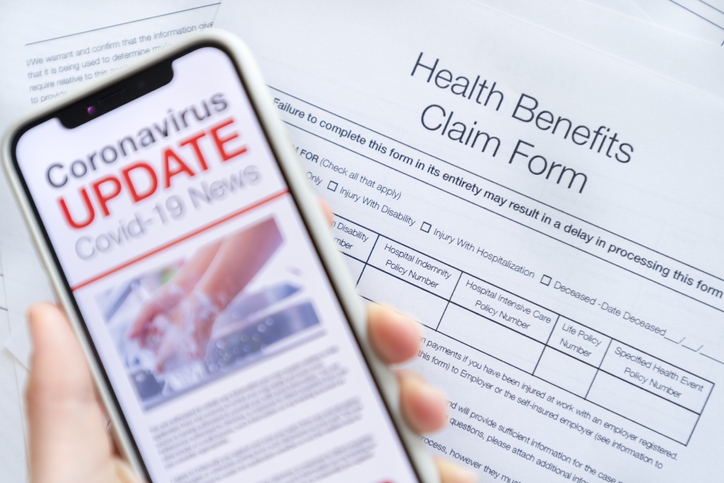 A person fills out a health insurance claim while reading COVID-19 news on a phone