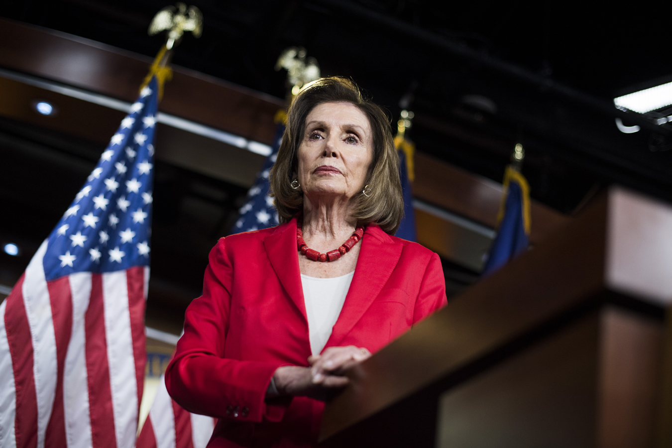 An image of Nancy Pelosi standing at a podium wearing a red blazer