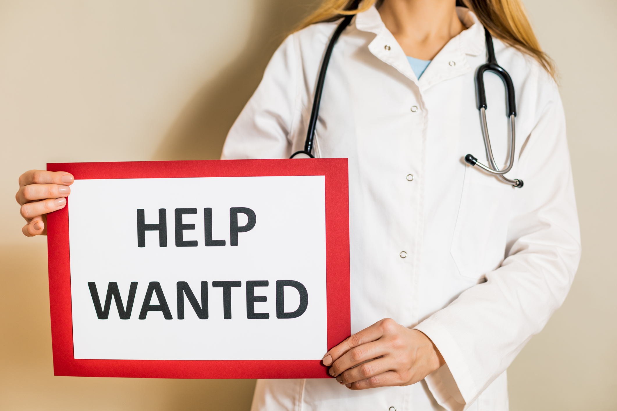A doctor holds a Help Wanted sign