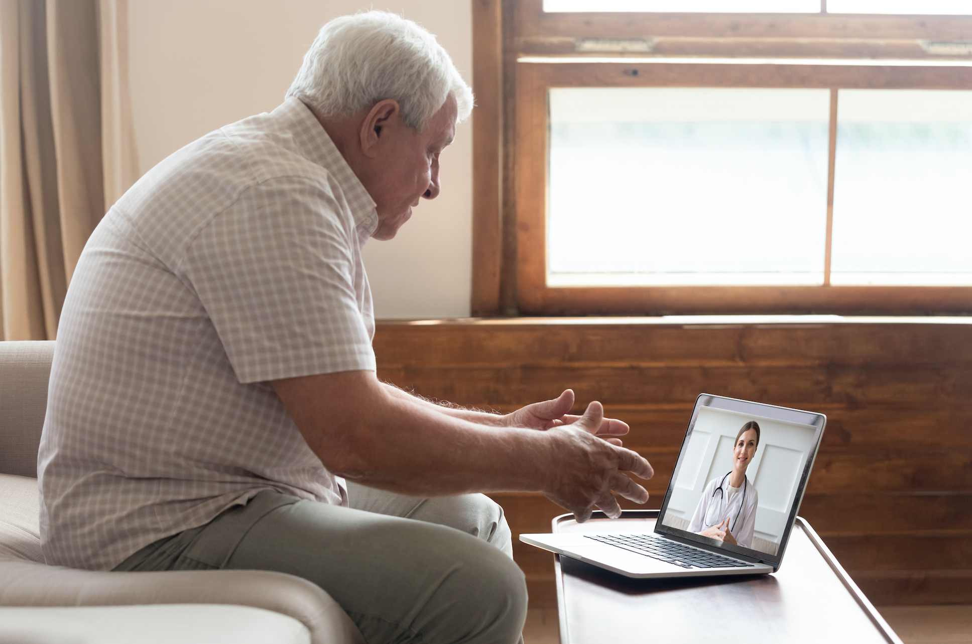An older man uses telehealth with a doctor on his laptop
