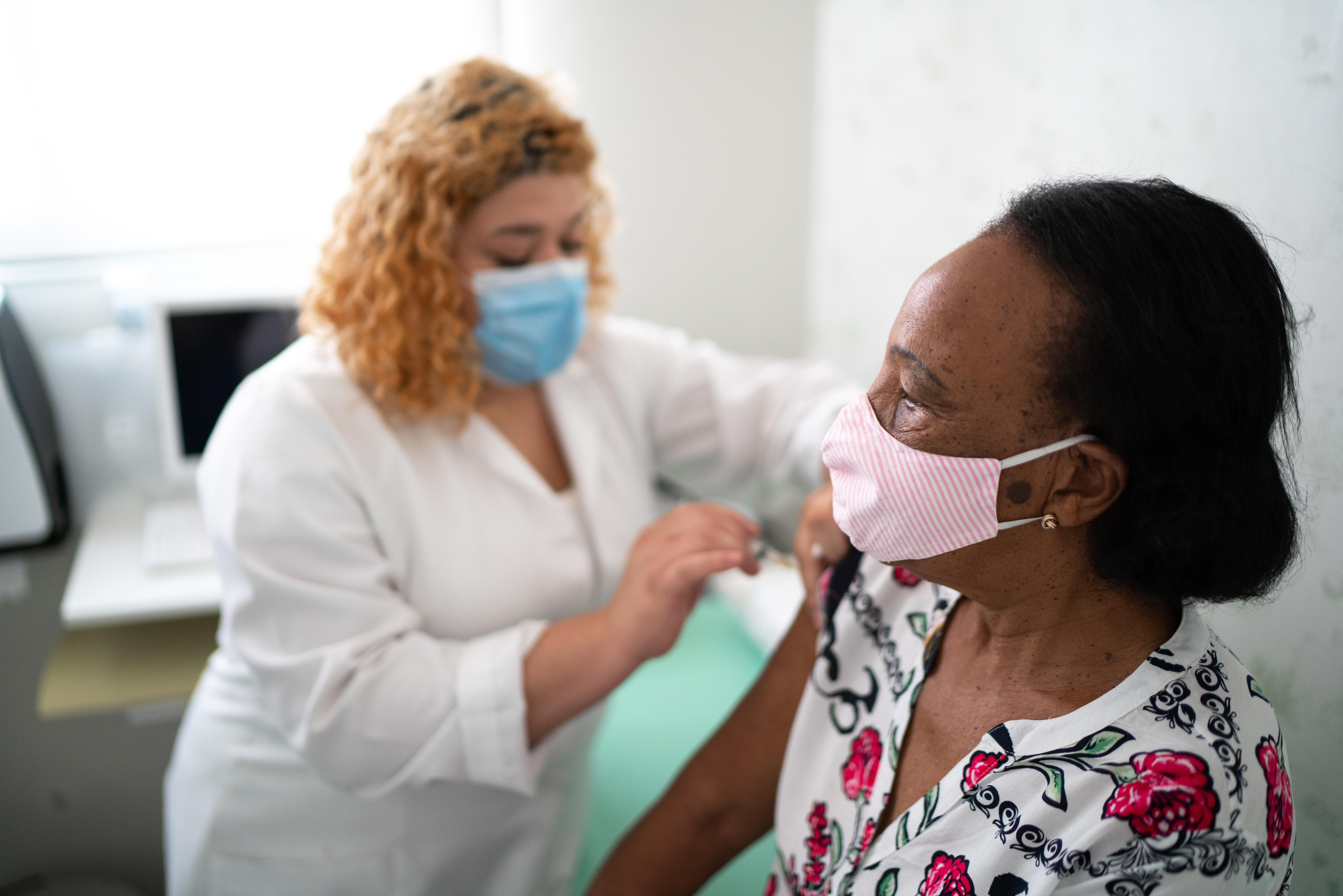 A woman in a mask gets a vaccine from a female health provider in a mask
