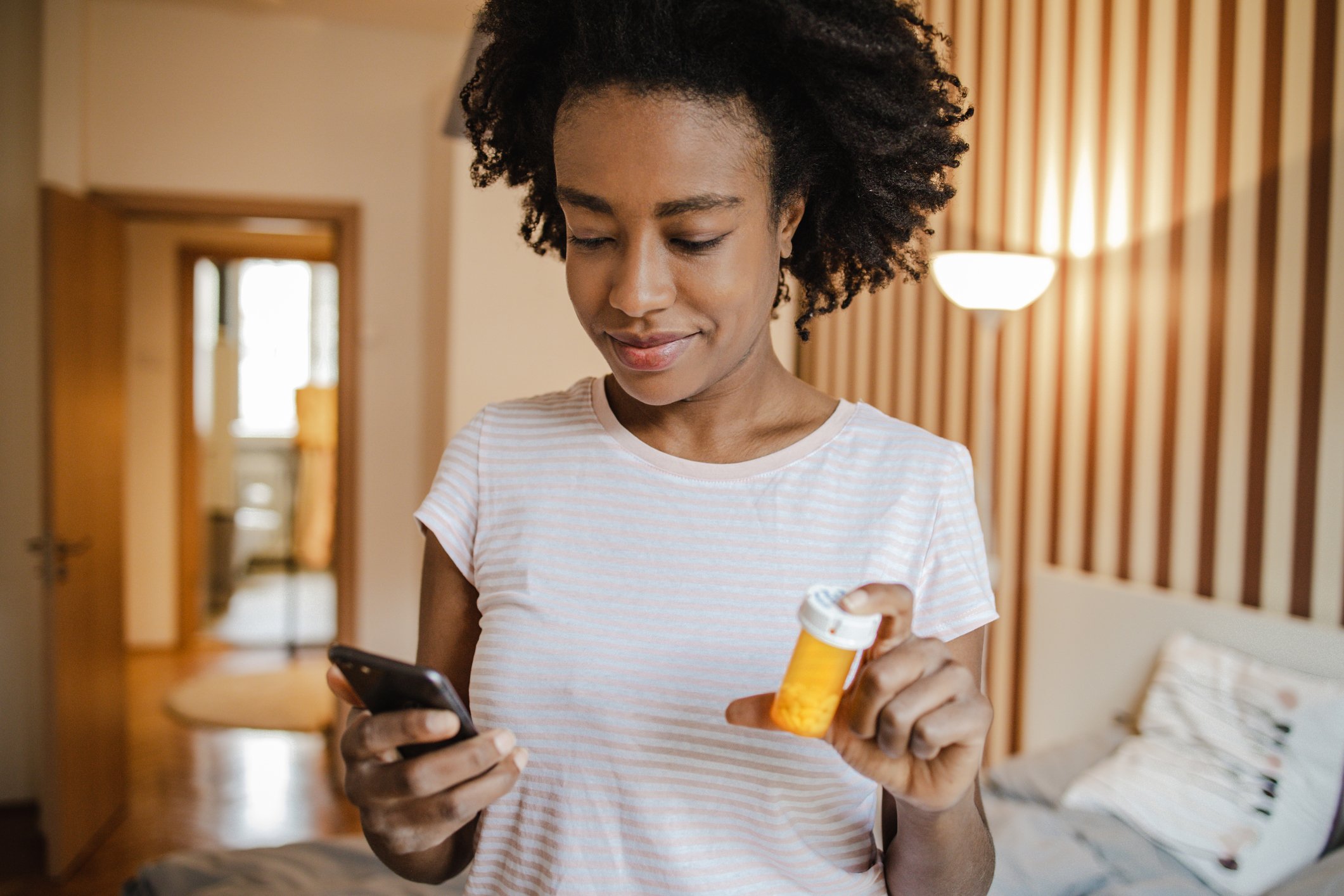 African American woman in the bedroom communicating with the doctor online while holding a bottle of medicine in her hand