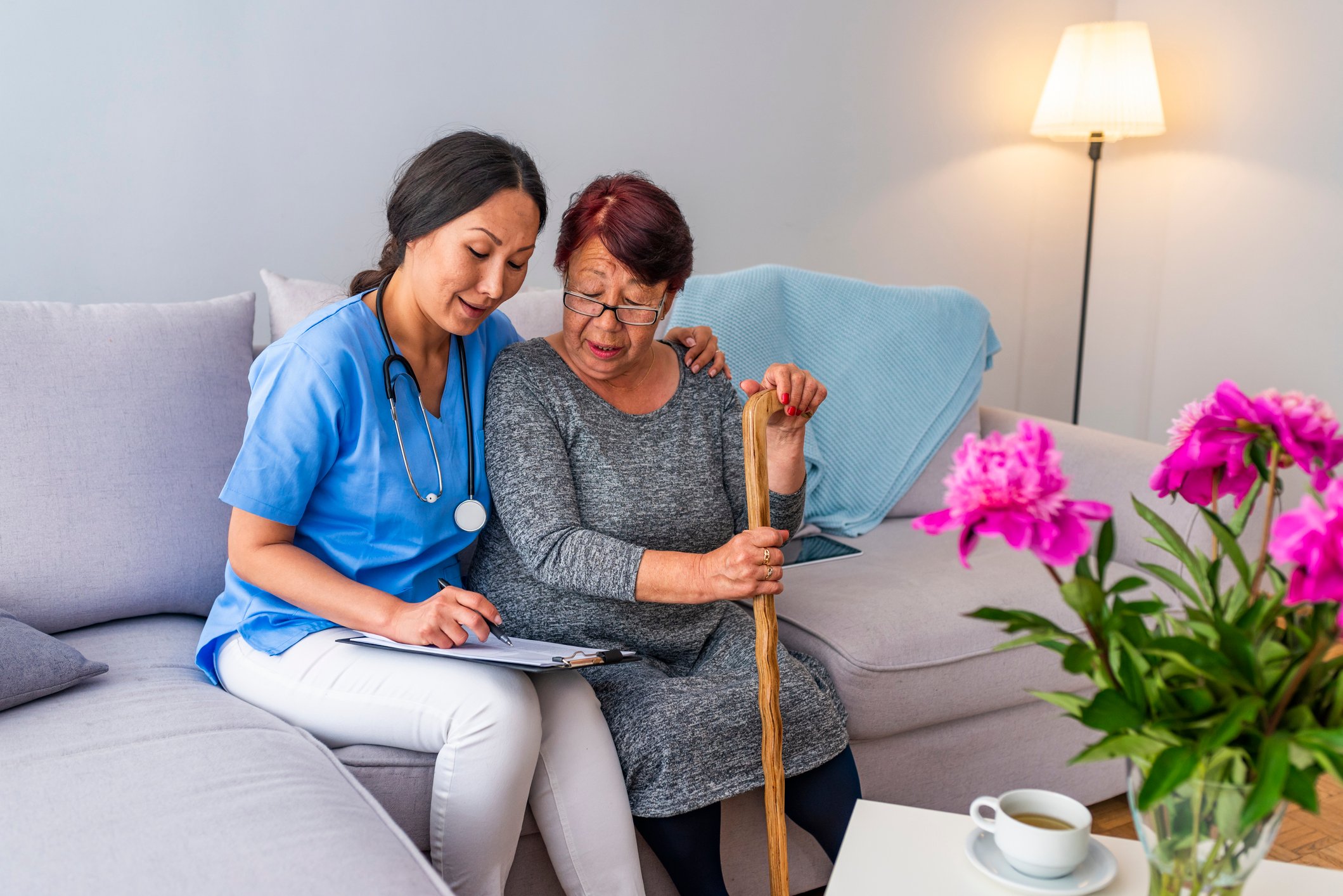 Smiling senior woman with walking stick and helpful caregiver holding her hand