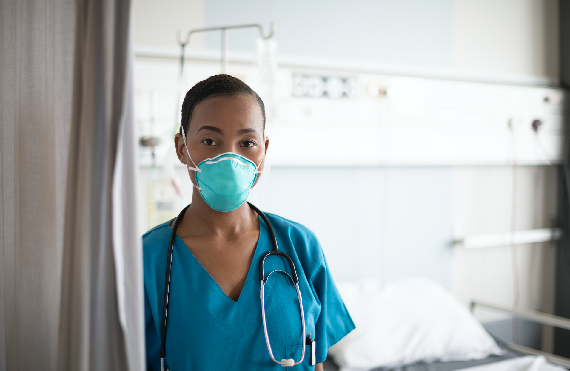 A female nurse is shown wearing an N95 mask in a hospital room