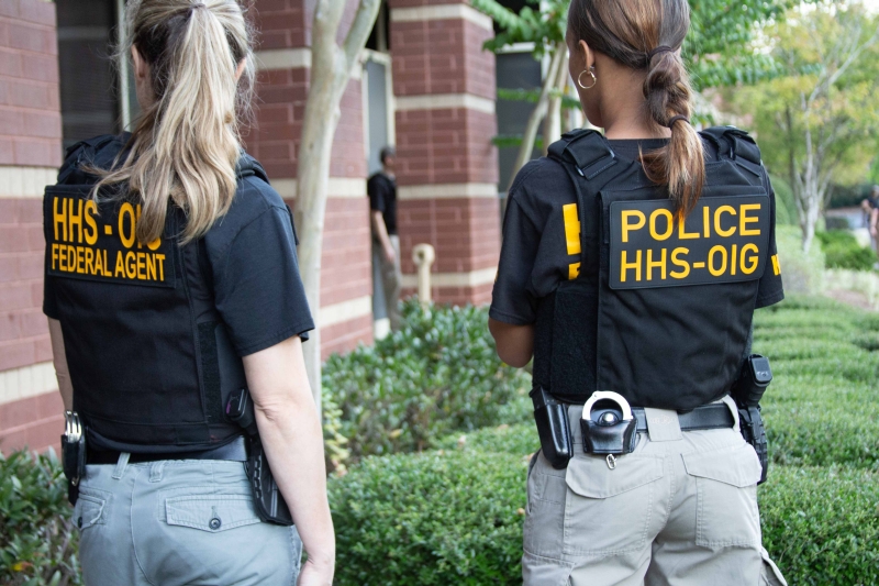 shows the backs of two female enforcement officers with Police HHSOIG insignia