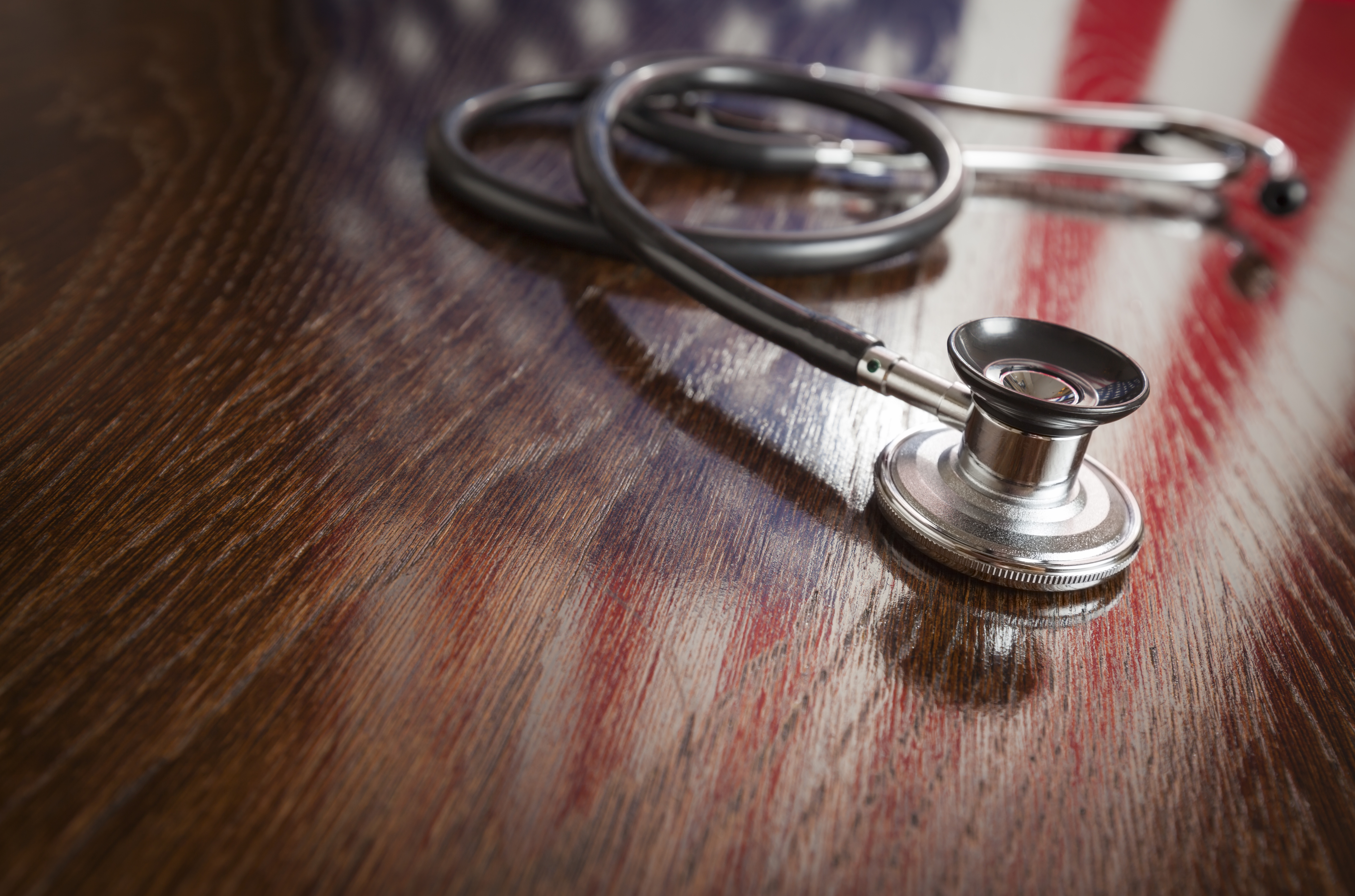 Stethoscope on wooden table with American flag reflected on the wood