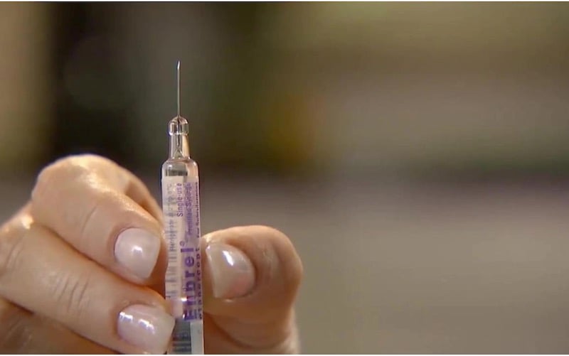 Closeup view of hand holding a prefilled syringe of Amgen drug Enbrel