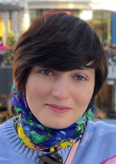 A headshot of Negin Majedi, Ph.D. Negin has brown hair and blue eyes. She wears a colorful scarf and a light blue sweater. 