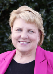 Carol Amick is shown wearing a pink blazer.