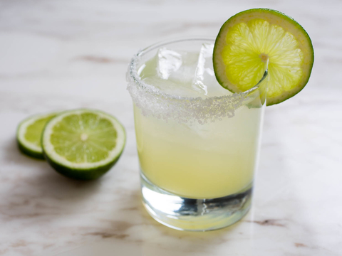 A glass with a green liquid, limes and ice in it