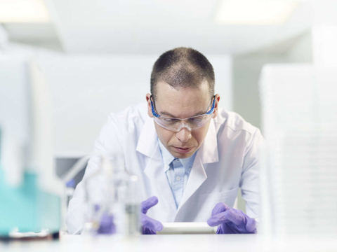 A man wearing a lab coat, purple medical gloves and eye protection