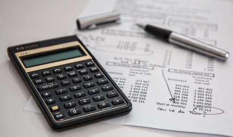 Calculator and pen sit on top of a spreadsheet of figures.
