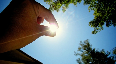 A hand that is positioned in front of the sun, as if pinching it
