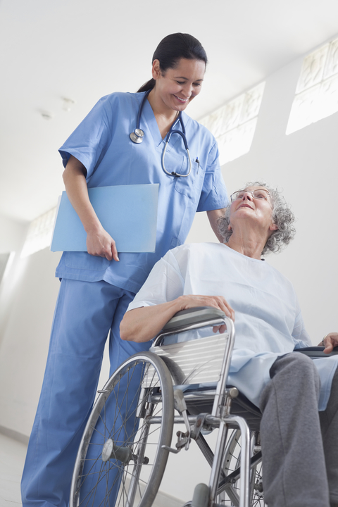 Nurse wheeling elderly patient down hall in wheelchair