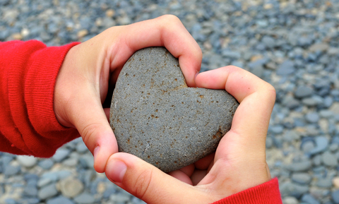 Hands holding a small rock shaped like a heart