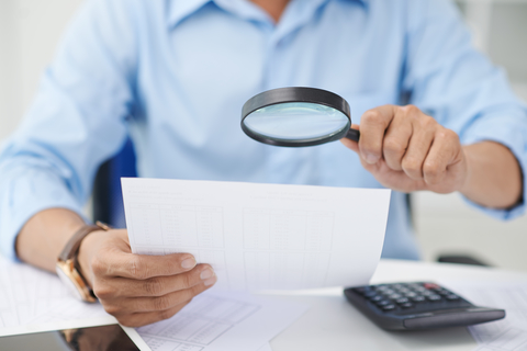 Fraud detection (CREDIT: Getty/DragonImages) Man using magnifying glass to look at paper