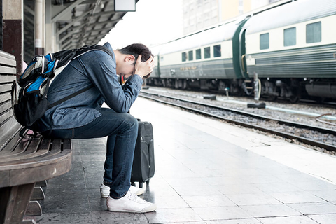 stressed traveler with head in hands outside at a train station