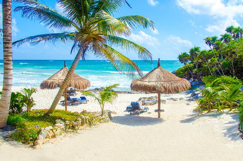 Tulum, Playa del Carmen // Photo by SimonDannhauer/iStock/Getty Images Plus/Getty Images Tulum beach with thatch umbrellas and lounge chairs