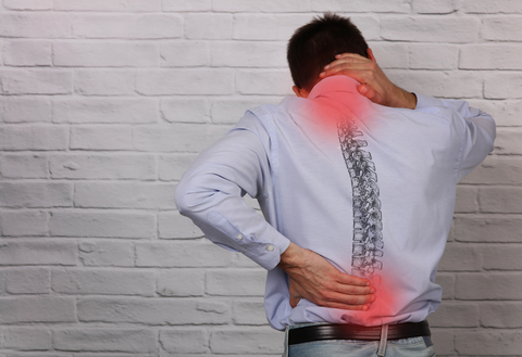 Back pain Back of man in long-sleeved shirt holding his neck and lower back. The places he's holding have red circles on them to indicate pain. An image of the spine is overlaid on his back.