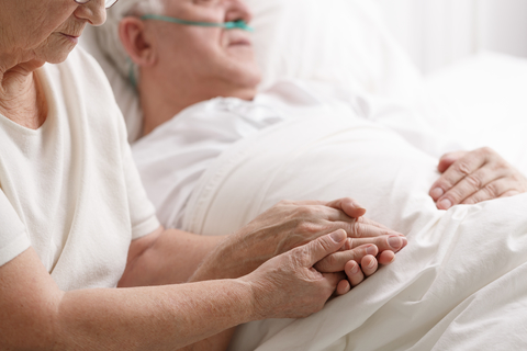 Senior couple in hospital Close up of senior woman holding senior man's hand at his bedside in a hospital setting