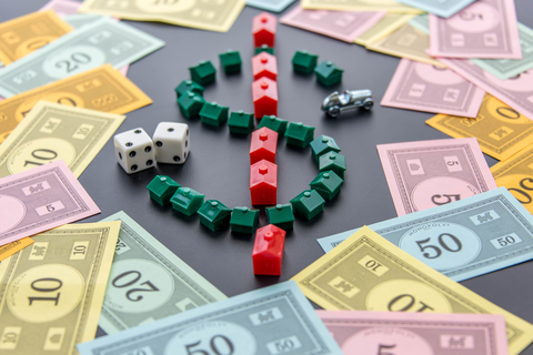 A dollar sign created by Monopoly game houses is surrounded by Monopoly money. Dice and the car token appear next to the dollar sign as well.