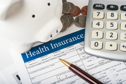 Paying for health insurance Health insurance form with wood pen, basic calculator, white piggy bank, and pile of coins