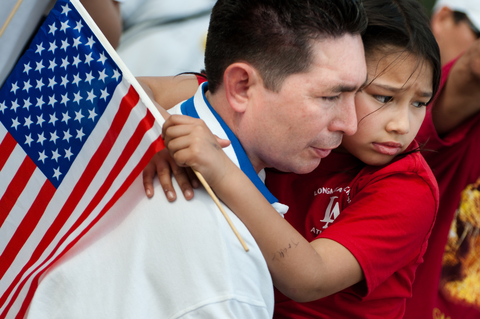Immigrant family members with U.S. flag Father and daughter with concerned looks on their faces; the father is holding the daughter and the girl is holding an American flag