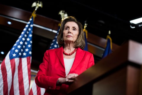 Nancy Pelosi An image of Nancy Pelosi standing at a podium wearing a red blazer.
