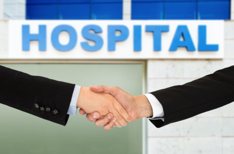 Hospital merger Photo of two men shaking hands in front of a hospital