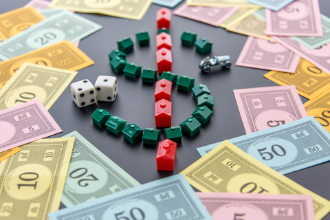 Monopoly money, cars, dice, hotels A dollar sign created by Monopoly game houses is surrounded by Monopoly money. Dice and the car token appear next to the dollar sign as well.