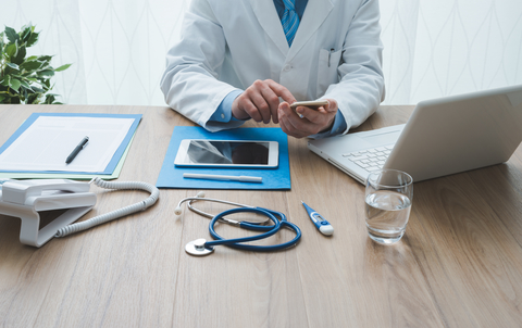 Doctor with patient file and technology Doctor at desk with notes, smartphone, tablet, computer, and stethoscope