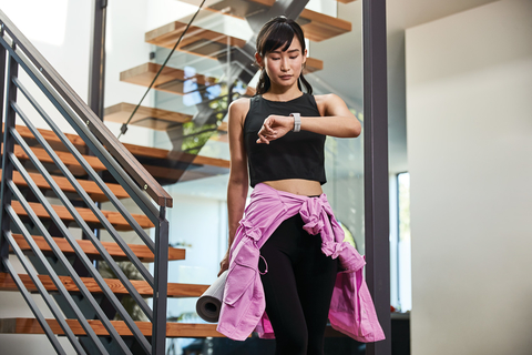 Fitbit fitness tracker woman dressed to exercise walks down stairs looking at Fitbit fitness tracker on her wrist