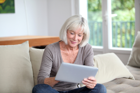 a senior woman sitting on a couch using a tablet