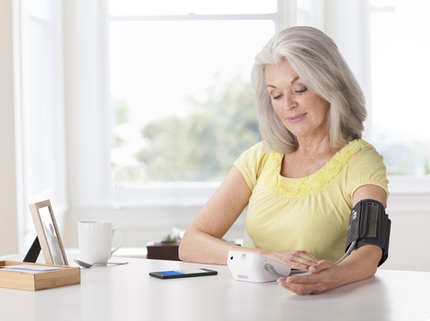 Livongo - woman using monitor Senior woman sitting at a table using blood pressure monitor device