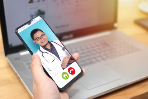 Telehealth A person talks to their doctor on their phone with a laptop in the background