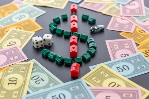 Monopoly money, cars, dice, hotels A dollar sign created by Monopoly game houses is surrounded by Monopoly money. Dice and the car token appear next to the dollar sign as well.