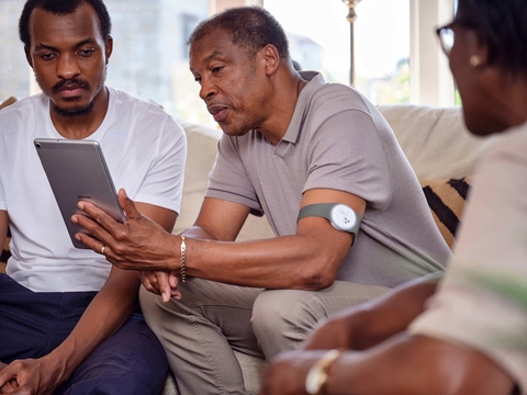 Current Health remote monitoring platform a male patient with a remote monitoring wearable on his arm uses a tablet to interact with his doctor