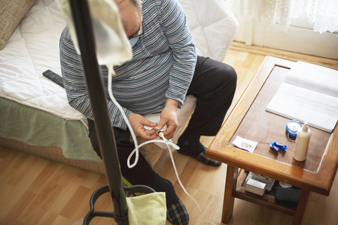 Senior man connecting peritoneal dialysis with catheter at home