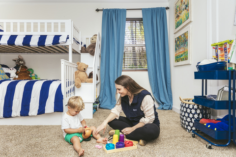 Sprout Therapy A female autism care therapist sits on the floor of a bedroom providing therapy services to a child