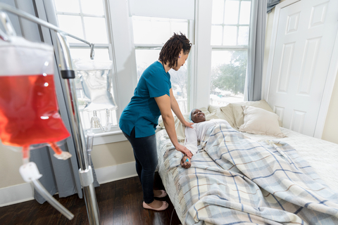 Home healthcare nurse visits with ill patient A caring female nurse helps a senior woman on hospice care. The nurse is checking the patient's pulse. An IV drip is in the foreground.