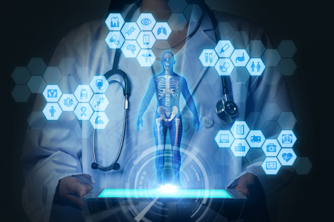 Digital health Physician wearing lab coat and stethoscope holding tablet. On top of tablet, there is a holographic skeleton diagram surrounded by hexagons with health symbols inside them, such as an ambulance, an x-ray, and a pill bottle.