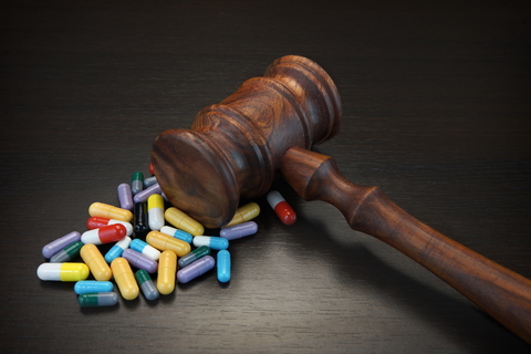 Drug lawsuit Wooden gavel over small pile of multi-colored pills on dark background.