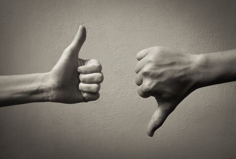 Black-and-white image of a thumbs-up hand and a thumbs-down hand in front of a blank wall.