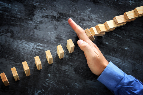 Hand stopping dominoes from falling Hand stopping the domino effect