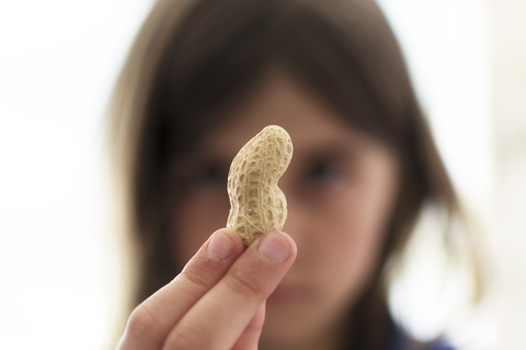 A young girl holding up a nut and looking sad Peanut